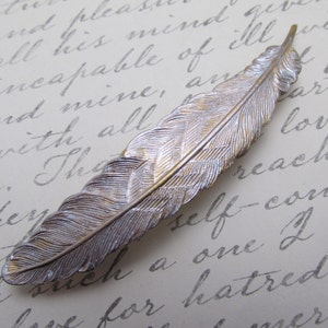 May include: A silver and gold feather-shaped hair clip. The feather has a detailed design and is a popular accessory for adding a touch of elegance to any hairstyle.