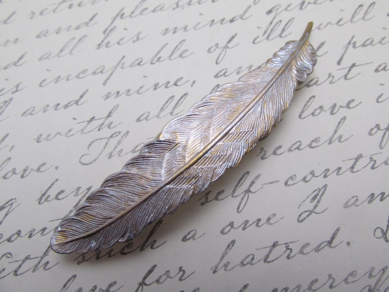 May include: A silver and gold feather-shaped hair clip. The feather has a detailed design and is a popular accessory for adding a touch of elegance to any hairstyle.