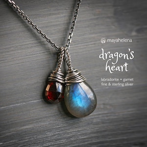 May include: A sterling silver necklace featuring two teardrop-shaped pendants. One pendant is a faceted, deep red garnet, and the other is a blue and gray labradorite. The necklace is labeled "dragon's heart."