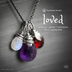 Op de afbeelding: Een zilveren ketting met drie edelsteen hangers: een paarse amethist, een rode granaat en een witte maansteen. De ketting is gemaakt van fijn en sterling zilver. De ketting is gelabeld met "loved" en "Mayahelena Jewelry".