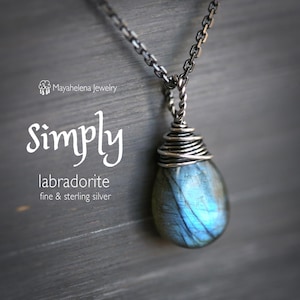 May include: A silver chain necklace with a teardrop-shaped labradorite gemstone pendant wrapped in silver wire. The pendant is a light blue color with iridescent flashes of color. The necklace is labeled "Simply labradorite fine & sterling silver".