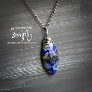 May include: A lapis lazuli pendant necklace with a sterling silver chain. The blue and gold gemstone is wire-wrapped and suspended from a delicate chain. The text "Simply" and "lapis lazuli fine & sterling silver" are visible.