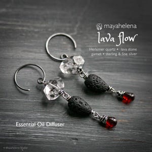 May include: A pair of handcrafted earrings featuring Herkimer quartz, lava stone, and garnet. The earrings have a silver wire design and a teardrop-shaped red garnet at the bottom. The text "Essential Oil Diffuser" is visible.