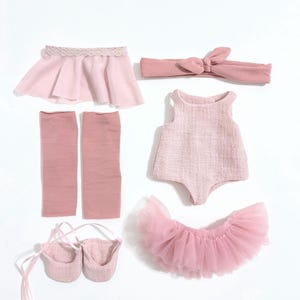 May include: A collection of pink doll clothing, including a skirt, headband, leg warmers, leotard, tutu, and ballet slippers. The items are arranged on a white background, showcasing a coordinated ballet-themed outfit.