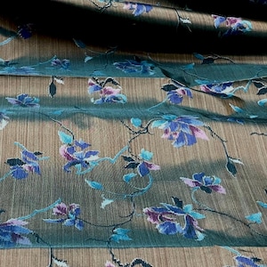 May include: A length of fabric featuring a dark brown base with a subtle horizontal texture. The material is decorated with a repeating pattern of small blue and purple flowers connected by thin, dark, winding vine-like stems throughout.