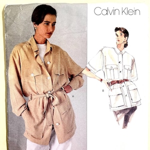 May include: A Vogue Patterns sewing pattern featuring a tan jacket with large pockets, a tie belt, and button closures. The pattern also includes a Calvin Klein design. The text "AMERICAN DESIGNER" is visible.