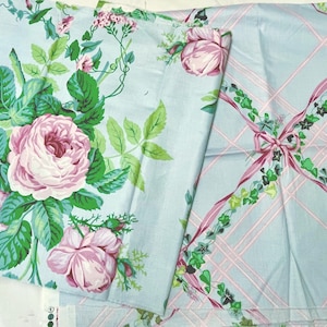 May include: Two pieces of fabric with floral and ribbon patterns. One features large pink roses with green leaves on a light blue background. The other has a light blue plaid design with pink ribbons and green ivy accents.