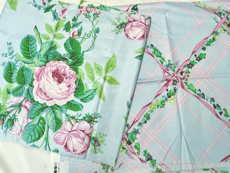 May include: Two pieces of fabric with floral and ribbon patterns. One features large pink roses with green leaves on a light blue background. The other has a light blue plaid design with pink ribbons and green ivy accents.