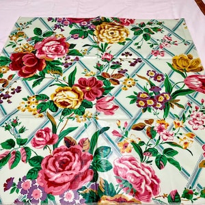 May include: A floral tablecloth featuring a repeating pattern of large roses in shades of red, pink, and yellow, interspersed with smaller flowers and green leaves. The background is a light green with a diamond grid pattern.