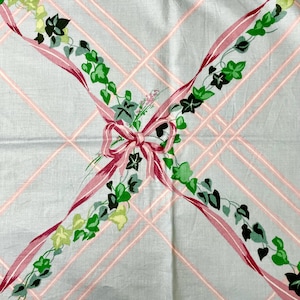 May include: A vintage light blue tablecloth with a pink plaid pattern. Pink ribbons with green ivy and a pink bow decorate the tablecloth. The tablecloth is made of a soft, possibly cotton, material.