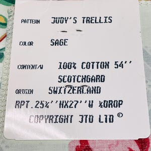 May include: A tag with the text "JUDY'S TRELLIS" and "SAGE" color. The tag also states "100% COTTON 54"" and "SCOTCHGARD". The origin is Switzerland. The fabric has a floral pattern with red, pink, and green colors.