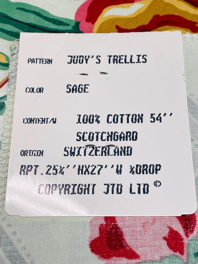May include: A tag with the text "JUDY'S TRELLIS" and "SAGE" color. The tag also states "100% COTTON 54"" and "SCOTCHGARD". The origin is Switzerland. The fabric has a floral pattern with red, pink, and green colors.