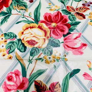 May include: A close-up of a floral pattern featuring large, colorful flowers in shades of red, pink, and yellow. The flowers are set against a white background with a light blue and white diamond pattern. Green leaves and stems complete the design.