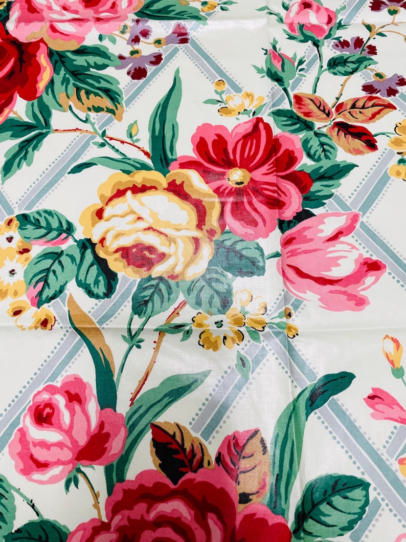 May include: A close-up of a floral pattern featuring large, colorful flowers in shades of red, pink, and yellow. The flowers are set against a white background with a light blue and white diamond pattern. Green leaves and stems complete the design.