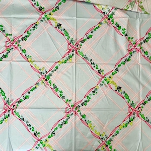 May include: Light blue fabric with a repeating pattern of pink ribbons, green vines, and bows. The design is arranged in a grid pattern with pink lines. The fabric appears to be cotton or a similar material.