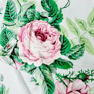May include: White fabric with a repeating floral pattern. Large pink roses with dark pink centers are surrounded by green leaves and vines. The design has a vintage, botanical feel.
