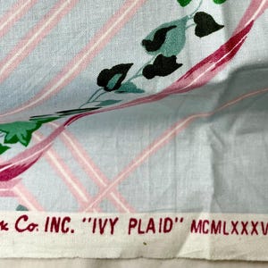 May include: Light blue fabric with a pink plaid pattern and floral accents. The fabric features a design of ivy leaves and pink ribbons. The text "Cyrus Clark Co. INC. 'IVY PLAID'" is printed at the bottom.