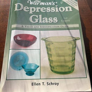 May include: A book titled "Warman's Depression Glass" with a green cover. The cover features images of Depression glass pieces in red, blue, and green. The book is a value and identification guide, 3rd edition, by Ellen T. Schroy.