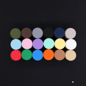May include: A collection of colorful, round objects arranged in rows on a black surface. The objects are in various colors, including green, brown, gray, black, blue, and white. The image is well-lit and the colors are vibrant.