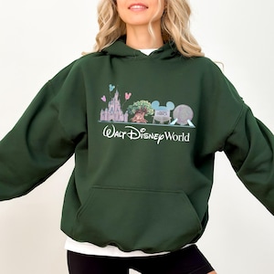 Op de afbeelding: Donkergroene hoodie met een voorzak en een wit ondershirt. De afbeelding op de voorkant toont een kasteel, boom, Mickey Mouse-hoofd en een bol, met de woorden "Walt Disney World" eronder.