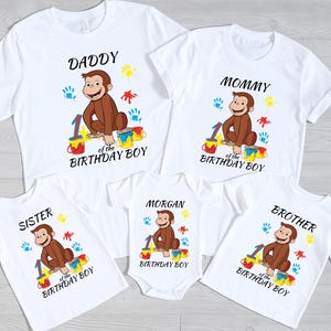 May include: White t-shirts and a onesie with a Curious George graphic. Each shirt has a different family member's name, the number 1, and the words "Birthday Boy". The shirts have colorful paint splatters.