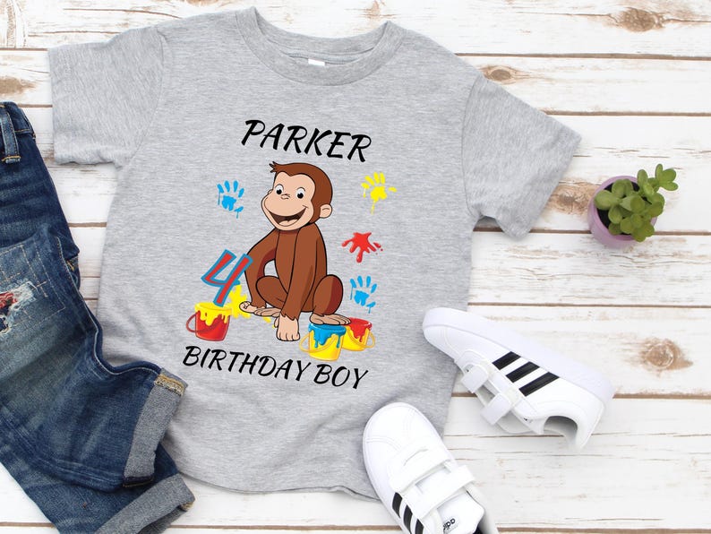May include: A gray t-shirt with a cartoon monkey design, the name "Parker", and the text "Birthday Boy". The design includes colorful paint splatters and the number 4. White sneakers and denim shorts are also visible.
