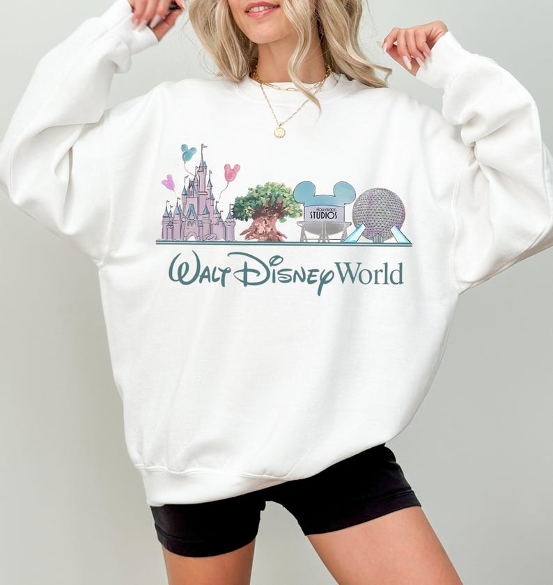 Op de afbeelding: Witte sweatshirt met een kleurrijke afbeelding van Walt Disney World-bezienswaardigheden, waaronder een kasteel, een boom en Spaceship Earth. De woorden "Walt Disney World" staan eronder in turquoise gedrukt. De sweatshirt is een comfortabele, casual stijl.