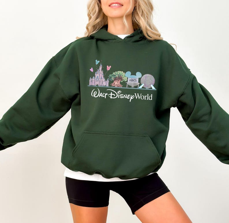 Op de afbeelding: Donkergroene hoodie met een voorzak en een wit ondershirt. De afbeelding op de voorkant toont een kasteel, boom, Mickey Mouse-hoofd en een bol, met de woorden "Walt Disney World" eronder.