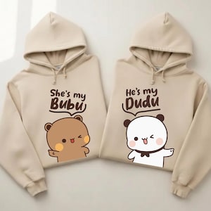 May include: Two beige hoodies with matching designs. One features a brown bear graphic and the text "She's my Bubu", the other has a panda graphic and the text "He's my Dudu". Both hoodies have drawstrings.