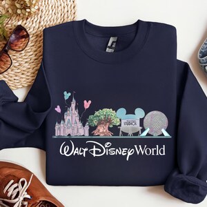 Op de afbeelding: Marineblauw sweatshirt met een kleurrijke afbeelding van Walt Disney World-bezienswaardigheden, waaronder een kasteel, een boom en Spaceship Earth. De woorden "Walt Disney World" staan eronder in witte letters. Een comfortabele, casual top.
