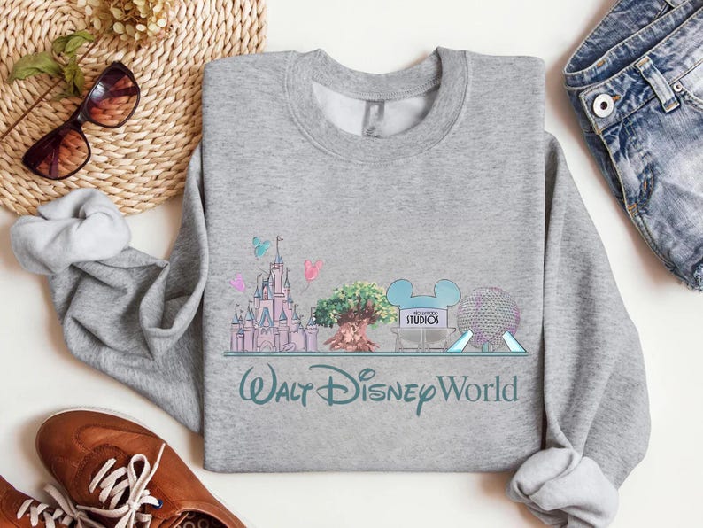 Op de afbeelding: Een grijze sweatshirt met een kleurrijke afbeelding van het Walt Disney World-logo en parkafbeeldingen. Het ontwerp omvat een kasteel, een boom en Spaceship Earth. De tekst "Walt Disney World" staat eronder.