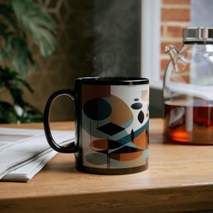 Könnte beinhalten: Eine schwarze Keramiktasse mit einem geometrischen Design mit abstrakten Formen in Braun-, Blau- und Schwarztönen. Die Tasse ist mit einem dampfenden Getränk gefüllt.