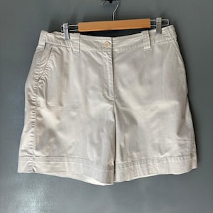 May include: A pair of light beige shorts with a button and zipper closure. The shorts have two front pockets and two back pockets.
