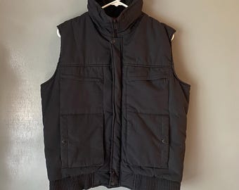 May include: A black quilted vest with a zipper closure and two large pockets on the front. The vest has a ribbed hem and collar.