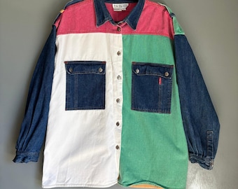 May include: A color-blocked button-down shirt with denim sleeves and pockets. The shirt features panels of pink, white, and green, with denim blue accents. Two denim pockets are on the front. The shirt is hanging on a black hanger.