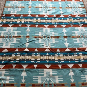 May include: A turquoise and brown patterned blanket with geometric designs. The blanket features repeating patterns of arrows, diamonds, and horizontal bands in shades of turquoise, brown, white, and tan. The blanket has a brown border.