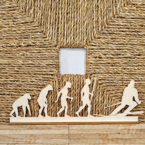 Könnte beinhalten: Eine Holz-Ausschneidung der Evolution des Menschen, beginnend mit einem Affen und endend mit einem Skifahrer. Die Ausschneidung befindet sich auf einem Holzgrund mit einem geflochtenen Seilmuster.