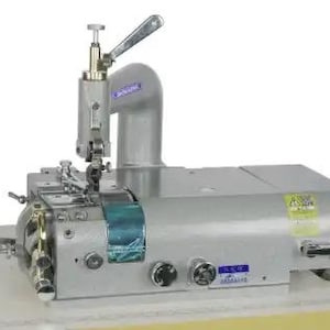 Pode incluir: Uma máquina de costura industrial prateada com uma etiqueta azul e branca. A máquina tem uma alavanca na parte superior e um pedal na parte inferior.