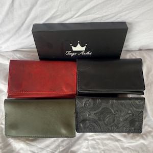 May include: Four leather wallets in different colors and textures. The wallets are arranged in a row on a white surface. The wallets are all closed and have a simple design. The wallets are labeled with the name "Tiago Andre" and a crown logo.