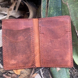 May include: A brown leather wallet with two pockets and a stitched edge.