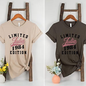 May include: Two t-shirts with the text "Limited Julia 1984 Edition" printed on them. One shirt is beige and the other is dark brown.