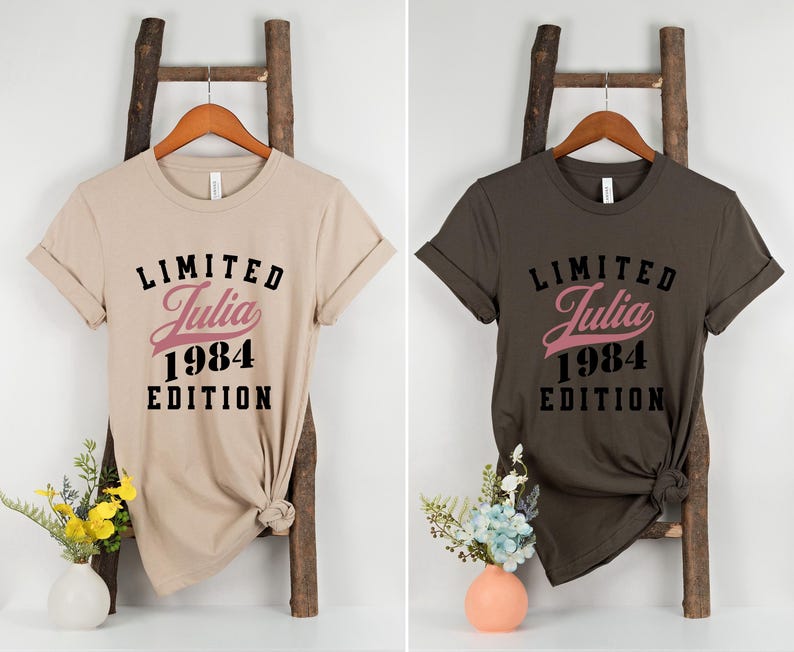 May include: Two t-shirts with the text "Limited Julia 1984 Edition" printed on them. One shirt is beige and the other is dark brown.