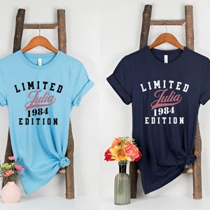 May include: Two t-shirts with a black and white graphic print. The text on the shirts reads "Limited Julia 1984 Edition". One shirt is light blue and the other is navy blue.