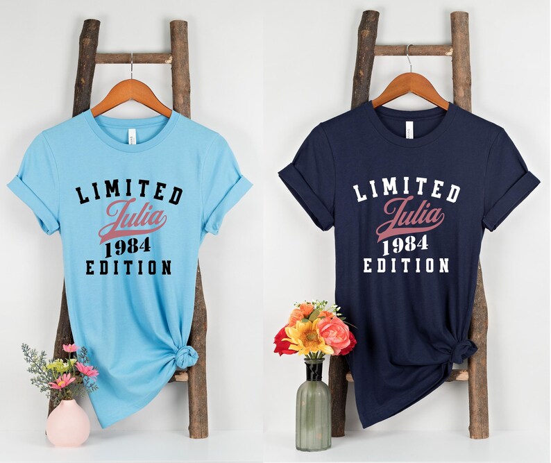 May include: Two t-shirts with a black and white graphic print. The text on the shirts reads "Limited Julia 1984 Edition". One shirt is light blue and the other is navy blue.