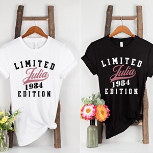 May include: Two t-shirts with a black and white graphic print. The white t-shirt has a pink "Julia 1984" text and the black t-shirt has a white "Limited Julia 1984 Edition" text.