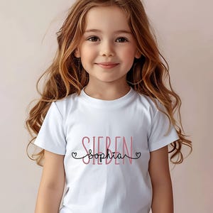 Peut inclure: T-shirt blanc avec le texte "Sieben" en noir et "Sophia" en rose avec des c&oelig;urs de chaque c&ocirc;t&eacute;.