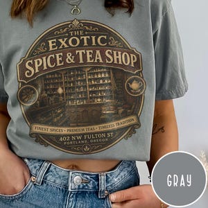 May include: A gray t-shirt featuring a circular graphic with the text THE EXOTIC SPICE & TEA SHOP, FINEST SPICES, PREMIUM TEAS, TIMELESS TRADITION, and 402 NW FULTON ST PORTLAND, OREGON. The illustration depicts a shop interior with shelves of jars.