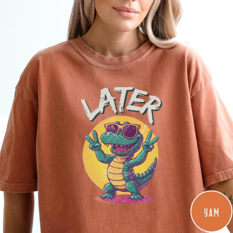 May include: A burnt orange t-shirt with a cartoon alligator wearing sunglasses and the word "LATER" printed on it.
