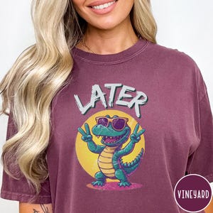 May include: A maroon t-shirt with a graphic of a green alligator wearing sunglasses and saying "Later".