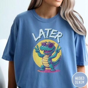 May include: A blue t-shirt with a cartoon alligator wearing sunglasses and the word "LATER" printed on it.